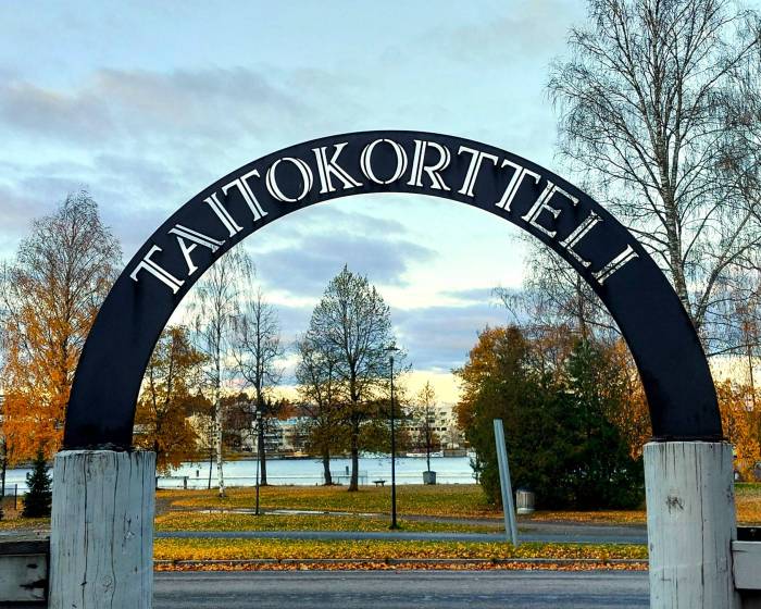Taitokorttelin portin takorautainen porttikaari taustalla syksyinen maisema